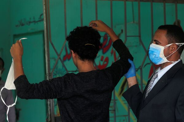 Охранник в защитной маске проверяет старшеклассника перед экзаменами в Каире, Египет - Sputnik Узбекистан