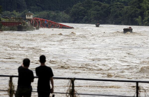 До сих пор 13 человек числятся пропавшими без вести. На фото - люди смотрят на вышедшую из берегов после сильных дождей реку Кумагава в городе Кумамура. Префектура Кумамото, юго-запад Японии - Sputnik Узбекистан