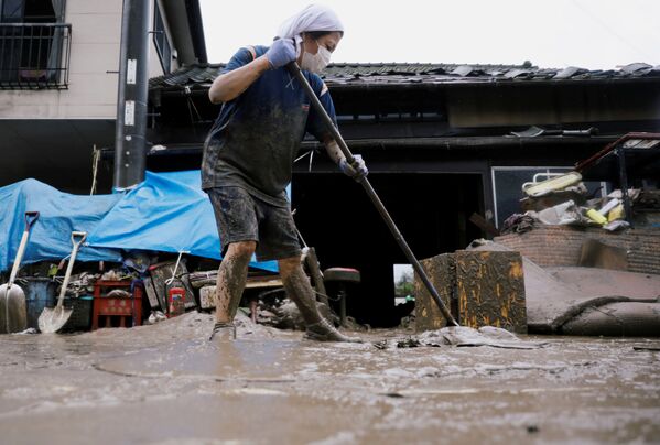 В результате наводнения люди, живущие в горных районах, остались без телефонной связи и водоснабжения. На фото - женщина пытается расчистить территорию у своего дома в городе Хитоёси в префектуре Кумамото, юго-запад Японии - Sputnik Узбекистан