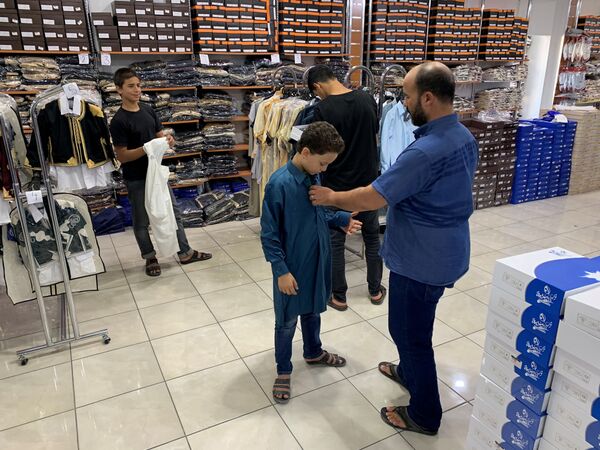 Мужчина примеряет своему сыну одежду в магазине перед празднованием Курбан-байрам в ливийском городе Мисрат - Sputnik Узбекистан