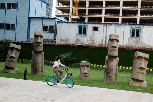 Pekinda Moai haykallari oldida ayol velosipedda o‘tib ketmoqda. - Sputnik O‘zbekiston