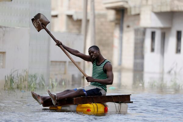 Мужчина на самодельном плоту с лопатой плывет по затопленным в результате проливных дождей улицам в Кеур-Массаре, Сенегал. - Sputnik Узбекистан
