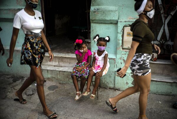 Девочки в масках ждут своих родителей, сидя на стуле в Гаване, Куба - Sputnik Узбекистан