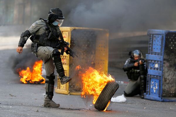 Офицер израильской полиции пинает горящую покрышку во время антиизраильской акции протеста в Хевроне на Западном берегу - Sputnik Узбекистан