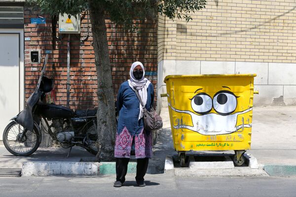 Женщина в защитной маске у разрисованного мусорного бака в Тегеране  - Sputnik Узбекистан