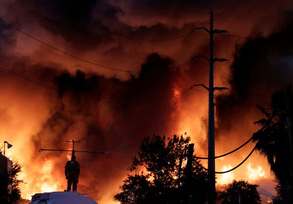 Пожарный стоит на резервуаре с водой во время пожара на заводе по переработке металлолома компании Deacero в Гуадалупе, Мексика. - Sputnik Узбекистан