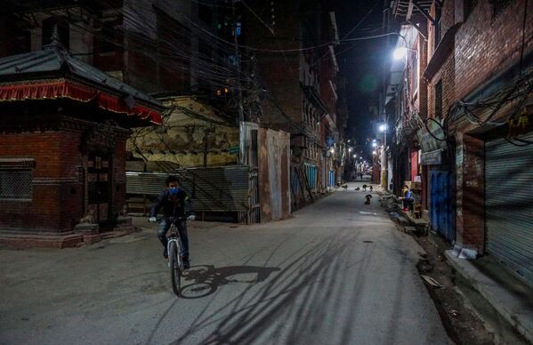 Мужчина в защитной маске едет на велосипеде по одной из улиц на окраине Катманду - Sputnik Узбекистан