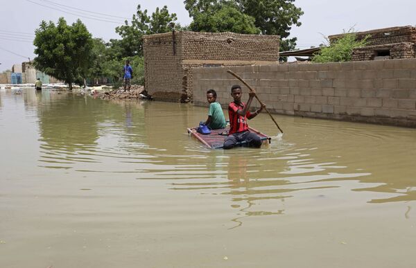 Подростки плывут на плоту по затопленной в результате наводнения улице в городе Салмания, Судан - Sputnik Узбекистан