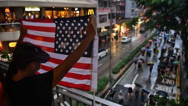 Мужчина держит флаг США над проходящими по улице Гонконга протестующими - Sputnik Узбекистан