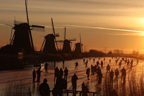 Люди катаются на коньках по замерзшему льду у ветряных мельниц в деревне Киндердейк, Нидерланды. - Sputnik Узбекистан