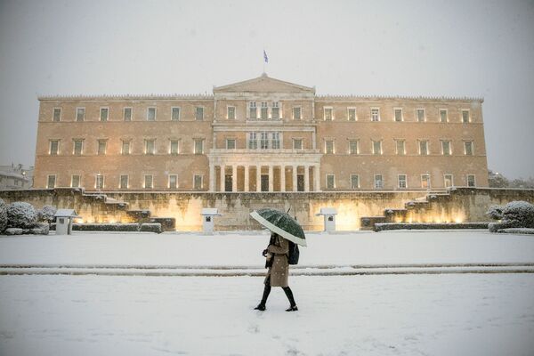 Женщина с зонтиком проходит мимо здания парламента во время сильного снегопада в Афинах, Греция - Sputnik Узбекистан