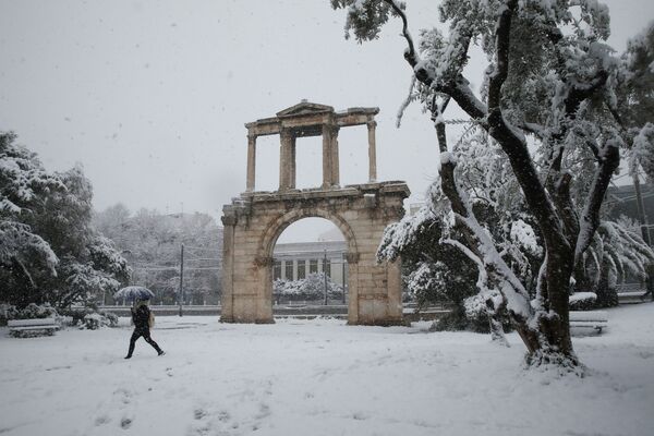 Пешеход идет рядом с воротами Адриана во время сильного снегопада в Афинах, Греция - Sputnik Узбекистан