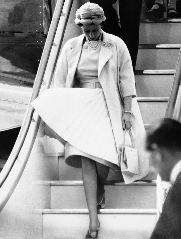 Королева Елизавета II, опустив глаза на свою развивающуюся на ветру юбку, выходит из самолета в аэропорту Лондона 2 августа 1959 года, завершая свой 45-дневный тур по Канаде. - Sputnik Узбекистан