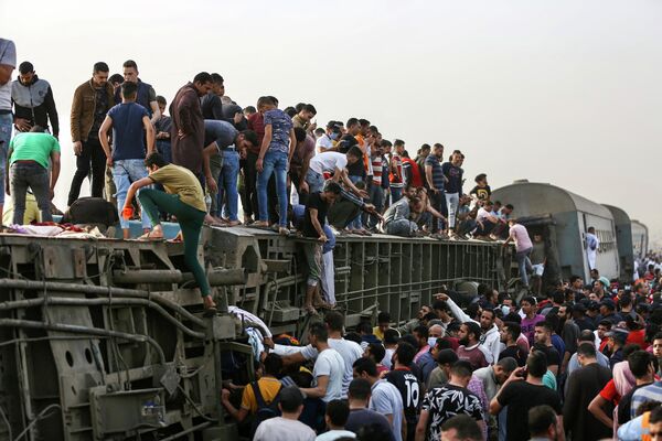 Люди забираются на перевернутый вагон на месте железнодорожной аварии в египетском городе Тух. - Sputnik Узбекистан