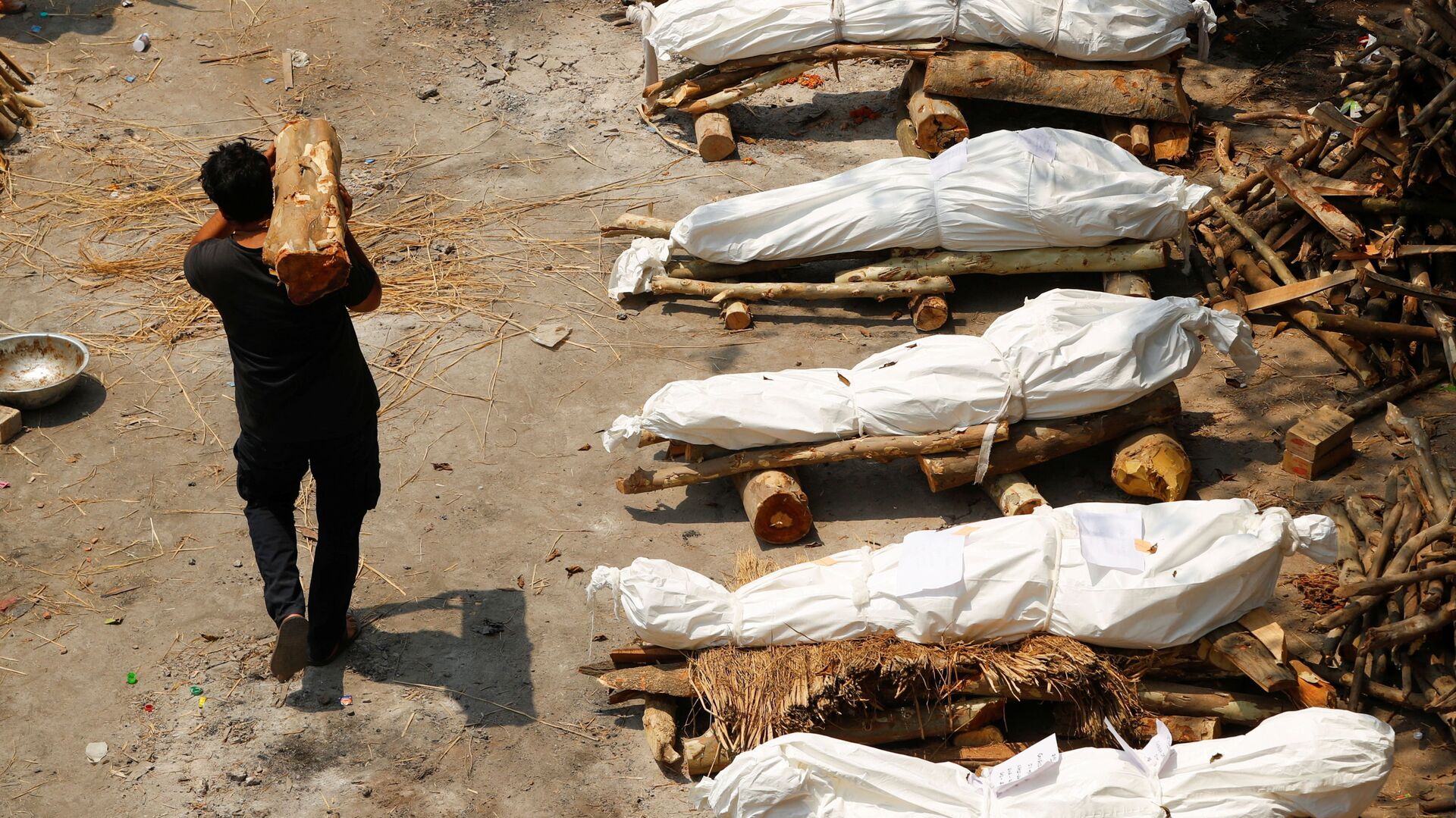 Мужчина с дровами проходит мимо погребальных костров во время массовой кремации в Индии - Sputnik Ўзбекистон, 1920, 05.08.2022