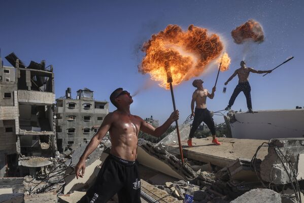 Палестинские спортсмены Bar Woolf из сектора Газа выступают с огнем над руинами здания, разрушенного в результате недавних израильских авиаударов в Бейт-Лахии. - Sputnik Узбекистан