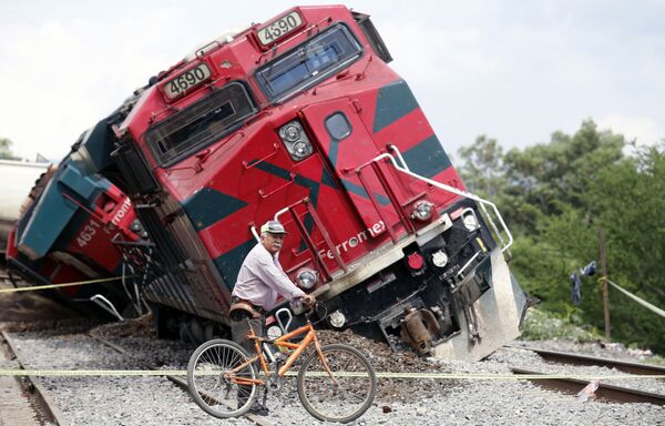 Велосипедист на фоне грузового поезда, который сошел с рельсов и врезался в жилые дома. Штат Халиско, Мексика. - Sputnik Узбекистан