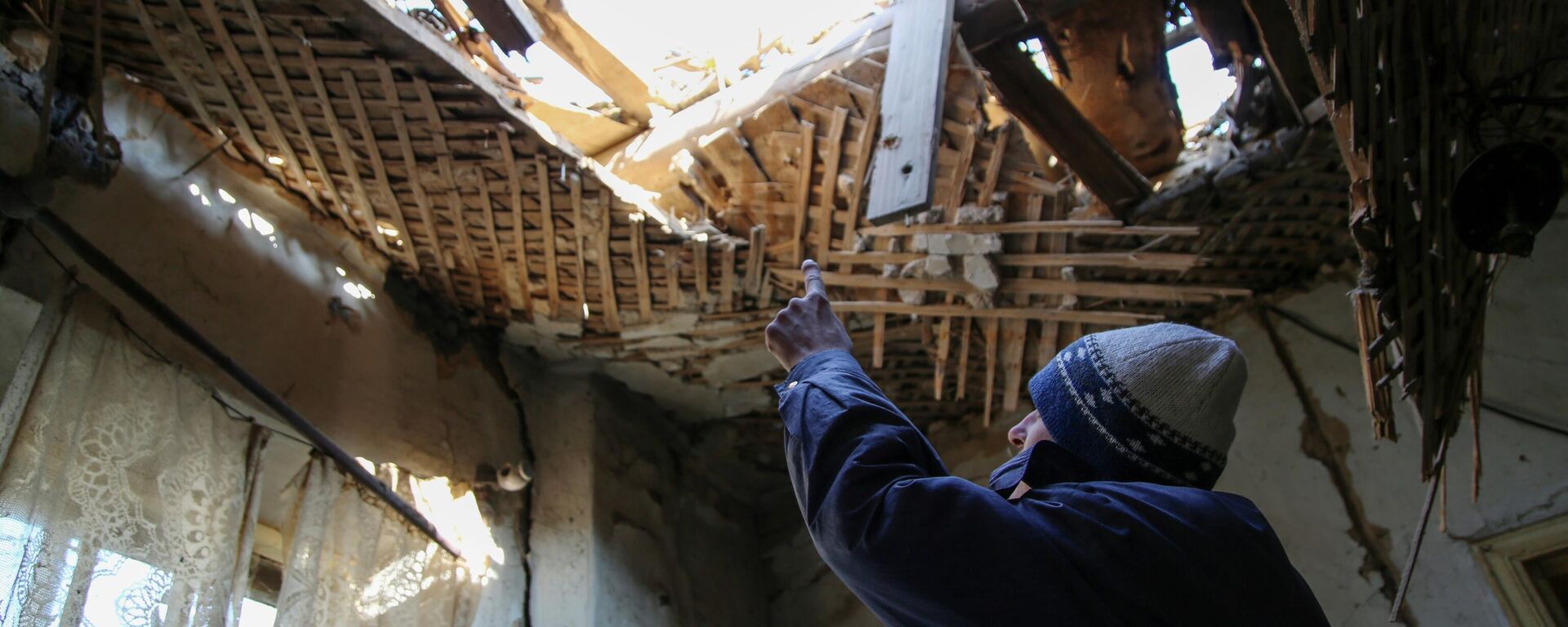 42-летний житель Донецка демонстрирует состояние своего дома на улице Дружбы, в крышу которого попал снаряд - Sputnik Узбекистан, 1920, 29.10.2021