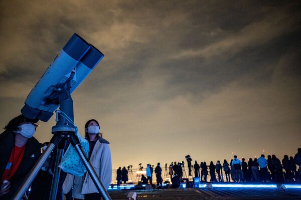 Люди наблюдают лунное затмение в телескоп на смотровой платформе в Токио. Это лунное затмение можно назвать &quot;почти полным&quot;, поскольку почти вся Луна зашла в тень Земли. Большая часть лунного диска приобрела  красноватый оттенок. - Sputnik Узбекистан