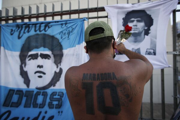 Мужчина прикрепляет цветок к футболке с изображением Марадоны во время демонстрации с требованием расследовать обстоятельства смерти футболиста 10 марта 2021 года. - Sputnik Узбекистан
