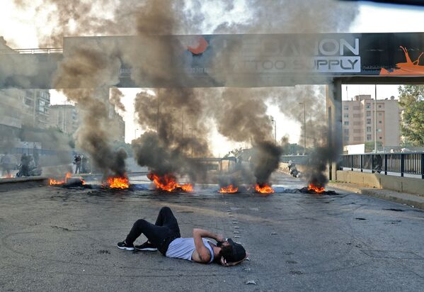 Протестующие в Ливане лежат на дороге, перекрытой горящими шинами, во время акции протеста в Бейруте 29 ноября, связанной с глубоким экономическим кризисом. - Sputnik Узбекистан