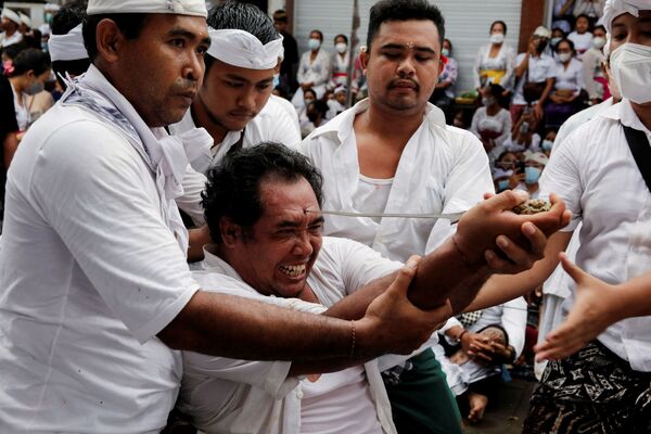 Мужчина на Бали пытается проткнуть лоб традиционным кинжалом во время священного ритуала Нгеребонг, Индонезия, 28 ноября 2021 г. - Sputnik Узбекистан