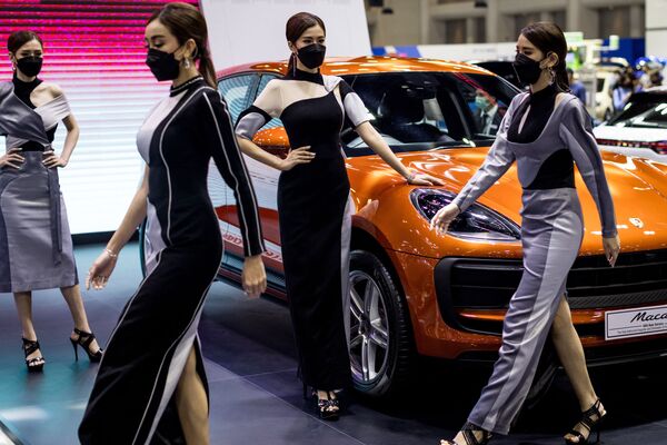 Модели проходят мимо автомобила Порш Макан на выставке Thailand International Motor Expo 2021 в Бангкоке 2 декабря 2021 г. - Sputnik Узбекистан