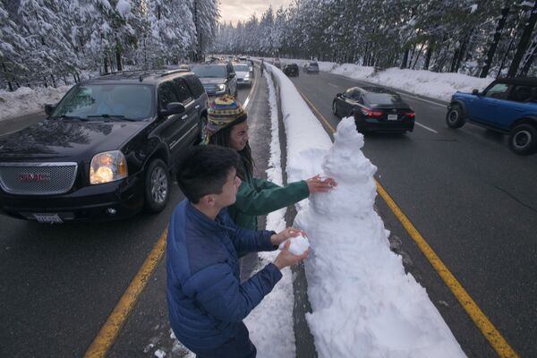 Люди лепят снеговика на разделительной полосе автодороги в Поллок Пайн, штат Калифорния, США, пока машины стоят в глухой пробке. - Sputnik Узбекистан