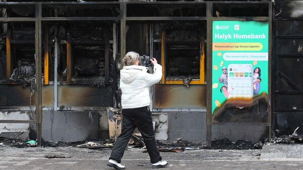 Женщина фотографирует здание, сожженное во время беспорядков в Алматы - Sputnik Ўзбекистон