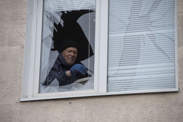Мужчина достает осколки из разбитого окна в жилом доме в городе Счастье в Луганской народной республике - Sputnik Узбекистан