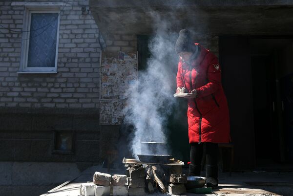 Женщина готовит еду на костре во дворе жилого дома в Волновахе - Sputnik Узбекистан