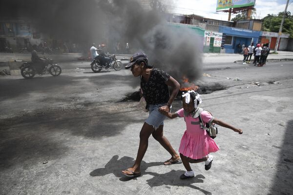 Женщина ведет ребенка мимо демонстрации против роста насилия в Порт-о-Пренсе, Гаити. - Sputnik Узбекистан