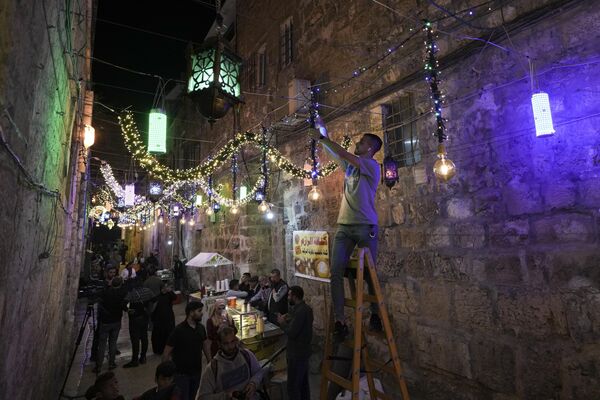 Мужчина в Старом Иерусалиме развешивает гирлянды в преддверии начала священного месяца Рамадан.  - Sputnik Узбекистан