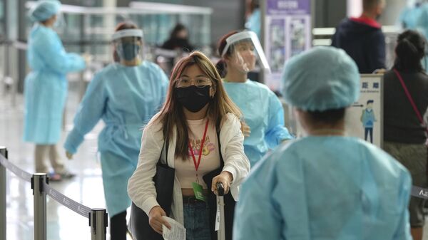Рабочие в защитных костюмах направляют пассажиров к автобусам в карантинные отели в аэропорту Гонконга - Sputnik Ўзбекистон
