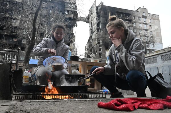 Mariupol aholisi ovqatni vayron bo‘lgan uy hovlisida pishirmoqda.  - Sputnik O‘zbekiston