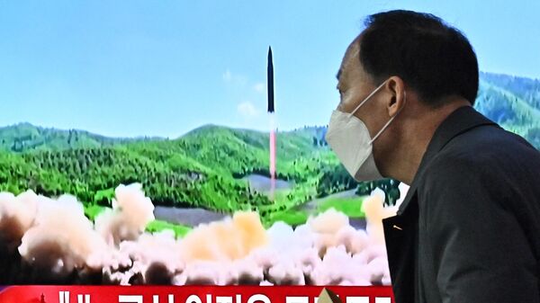Мужчина проходит мимо экрана телевизора с выпуском новостей с кадрами испытания северокорейской ракеты - Sputnik Ўзбекистон