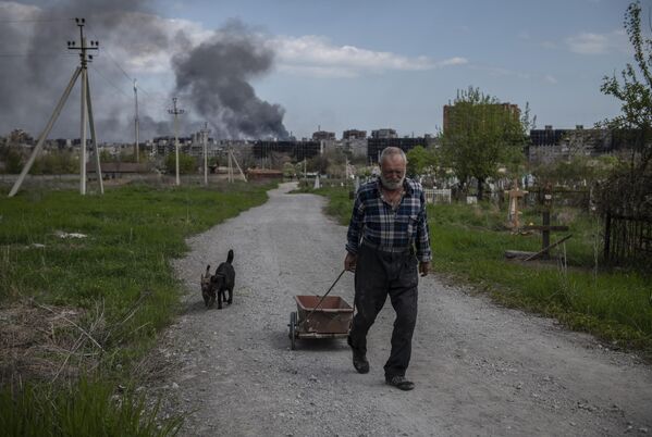 Мужчина везет тележку с травой неподалеку от металлургического комбината Азовсталь в Мариуполе - Sputnik Узбекистан