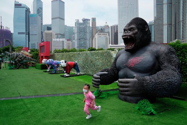 Девушка в маске &quot;убегает&quot; от статуи Кинг Конга в парке в Гонконге. - Sputnik Узбекистан