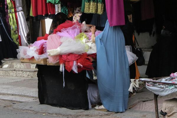 Женщина в бурке рассматривает детскую одежду в Герате. - Sputnik Узбекистан