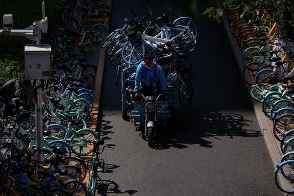 Рабочий едет мимо рядов неиспользуемых из-за изоляции общих велосипедов, припаркованных вдоль улицы в районе Чаоян в Пекине. - Sputnik Узбекистан