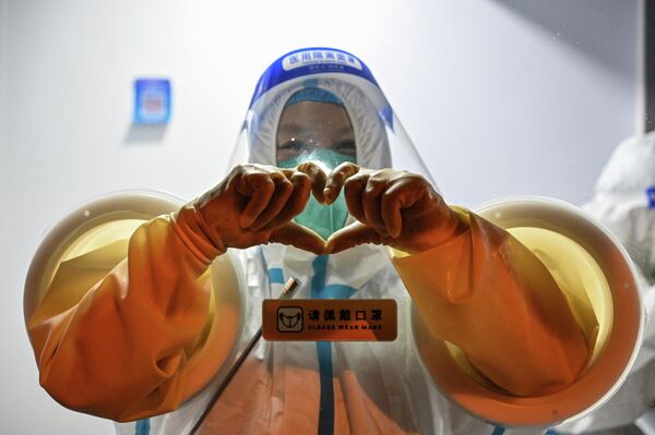 Медицинский работник делает руками сердце, ожидая взятия образцов мазков у людей в районе Цзин в Шанхае 31 мая 2022 года, когда город готовится снять новые ограничения. - Sputnik Узбекистан
