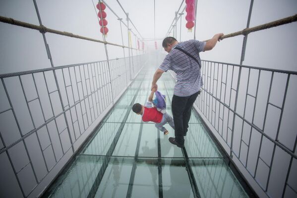Китайский турист держится за своего сына, когда они идут по подвесному мосту со стеклянным дном в горах Синючжай в уезде Пинцзян, провинция Хунань, примерно в 150 километрах от Чанши, 7 октября 2015 года. Первоначально мост представлял собой деревянную дорожку шириной около 300 метров. 180-метровая долина, вновь открытая две недели назад после реконструкции в качестве туристической достопримечательности со стеклянным дном. - Sputnik Узбекистан