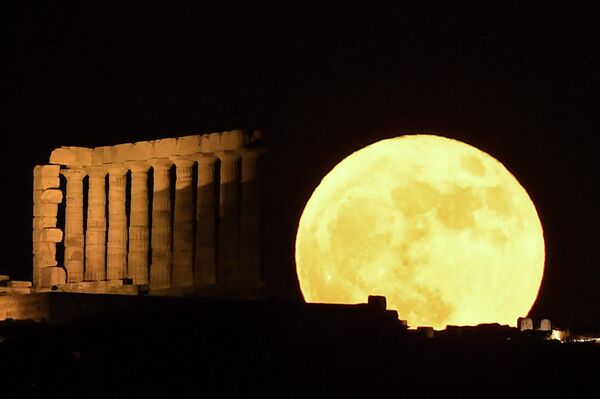 На этой фотографии изображена полная луна, известная как &quot;клубничная луна&quot;, за храмом Посейдона на мысе Сунион, к югу от Афин, 14 июня 2022 года. - Sputnik Узбекистан