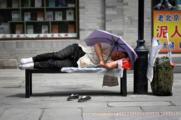 Мужчина спит на скамейке под зонтиком около дороги в Китае, 30 июня 2022 года. - Sputnik Узбекистан