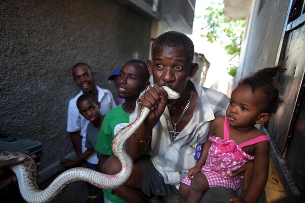 На этой фотографии, сделанной 27 января 2013 года, мужчина целует змею на удачу после того, как заплатил дрессировщику змей Сентилусу Ресилусу, выступающему на улице во время карнавала перед Великим постом в Петионвилле, Гаити. Это змеи помогают Ресилусу оплачивать жилье и квартиру. - Sputnik Узбекистан