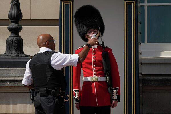 Полицейский подает воду британскому солдату в традиционной шапке из медвежьей шкуры. Он несет караул у Букингемского дворца. - Sputnik Узбекистан