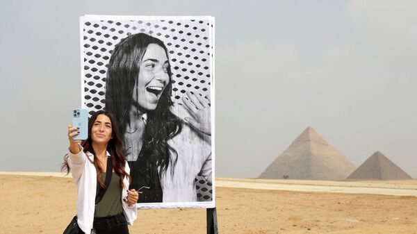 Египтянка делает селфи перед своей фотографией, напечатанной в фотобудке на плато Пирамид в Гизе - Sputnik Узбекистан
