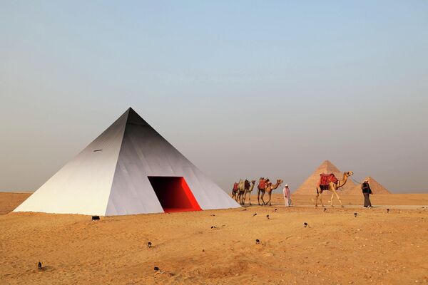 Караван верблюдов проходит мимо интерактивной фотобудки в форме пирамиды французского архитектора  JR. - Sputnik Узбекистан