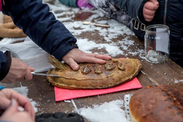 Мужчина разрезает пирог с начинкой из целой рыбы с торчащим хвостом на конкурсе-дегустации национальной карельской выпечки на рыболовном фестивале Пудожские налимы - Sputnik Узбекистан