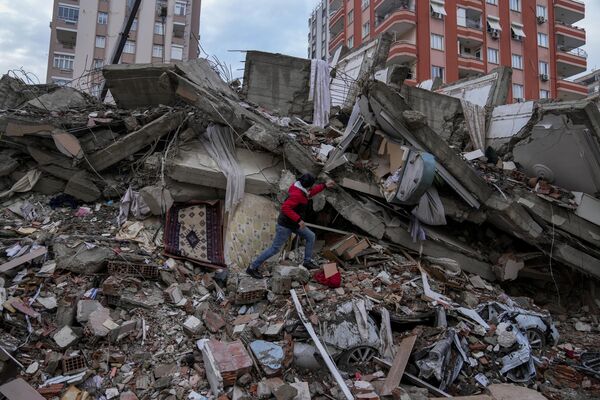 Мужчина в поисках людей в разрушенном здании в Адане, Турция, понедельник, 6 февраля 2023 года. - Sputnik Узбекистан